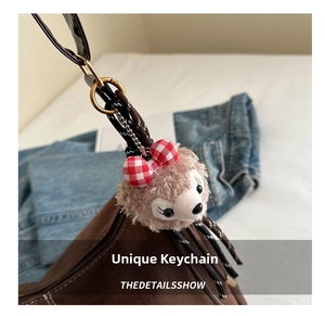 Close-up of a cute brown plush bear charm with a red checkered bow on a tote bag