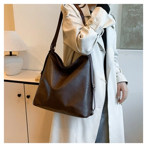Vue détaillée du grand sac cabas en cuir marron foncé porté avec un manteau blanc