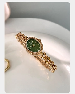 Macro shot of elegant gold vintage watch with emerald green dial on white ceramic tray
