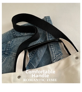 Detail of canvas tote bag with black webbing handles and reinforced metal rivets