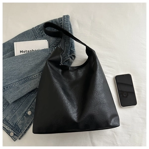 Détail du sac cabas en simili cuir noir avec texture froissée sur fond de tissu blanc