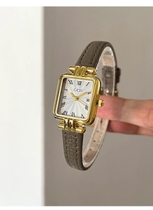 Dettaglio dell'orologio GEDI rettangolare dorato con cinturino in pelle grigia e numeri romani