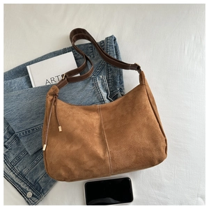Close-up of brown suede hobo bag with drawstring detail and leather strap on white fabric