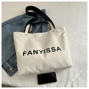 Detail of white canvas tote bag with FANYISSA print and black wide shoulder strap