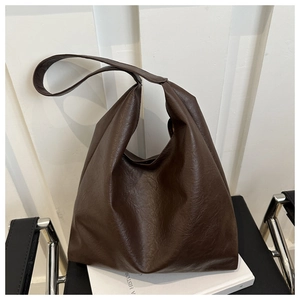 Detail of soft dark brown leather tote bag with wide shoulder strap on a black chair