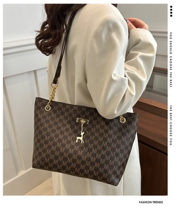 Detail of brown monogram tote bag with golden metal deer charm and textured chain strap
