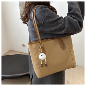 Close-up of light brown tote bag featuring contrast white stitching and plush monster charm