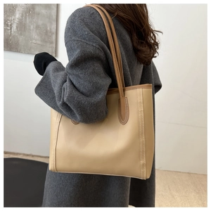 Detail view of large khaki tote bag with brown trim and white contrast stitching on model