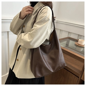 Grand sac hobo marron foncé porté par un mannequin avec une veste beige dans un décor épuré
