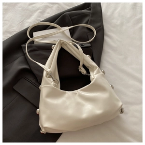 Close-up of cream leather shoulder bag with silver rivet details on a gray blazer