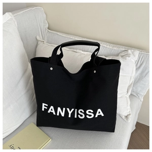 Close-up of a large black canvas tote bag with white lettering on a soft white sofa