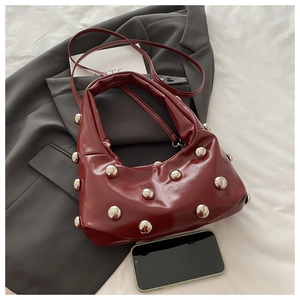 Detail of burgundy leather shoulder bag with silver rivet studs on a gray blazer