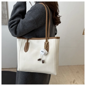 Detail of white tote bag featuring brown straps and a cute plush doll charm
