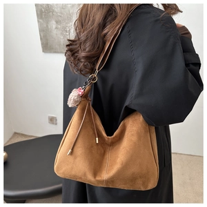 Detail of a brown suede tote bag with a soft plush keychain charm and gold metal rings