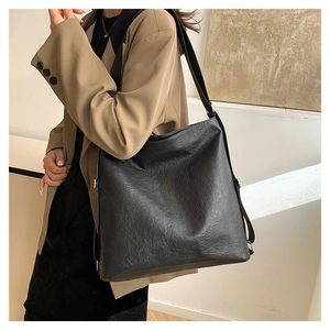 Detail of black faux leather tote bag with wide strap in a minimalist setting