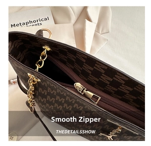 Close-up of golden zipper hardware and M-pattern print on dark brown tote bag