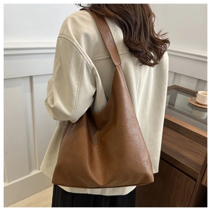 Sac hobo minimaliste marron foncé porté par un mannequin dans un décor intérieur