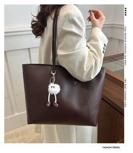 Macro view of a large dark brown tote bag with a white plush charm and matte texture