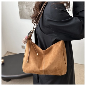 Detail of a brown suede crescent underarm bag with decorative stitching and fur pompom