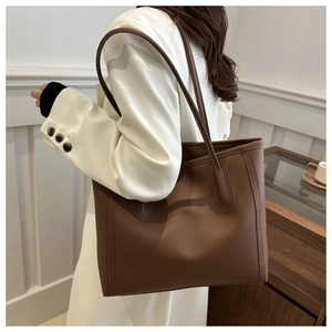 Close-up of brown matte leather tote bag worn with a blazer for a professional look