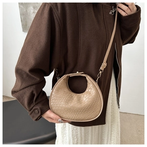 Détail du sac croissant marron clair à texture crocodile porté avec un manteau brun