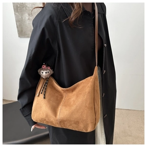 Detail of brown suede tote bag featuring plush charm on black coat styling