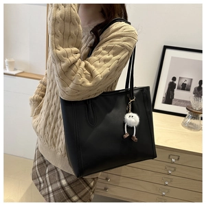 Close-up of black leather tote bag with stitching detail and plush charm on casual outfit