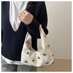 Detail of white pleated handbag with silver rivet studs held by model for style view