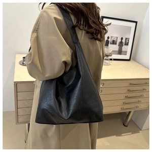 Detail of a large black faux leather tote bag with soft pleated texture on a trench coat