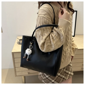 Detail of black leather tote bag with plush charm accessory worn by model in home setting