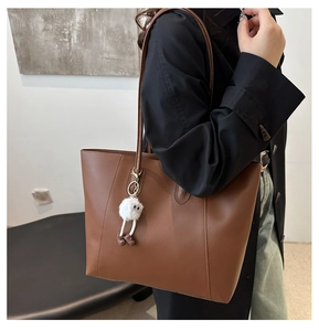 Detailed texture of dark brown leather tote bag with cute white plush monster charm accessory