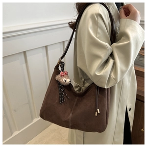 Detailed close-up of brown suede tote bag with contrast stitching and plush charm