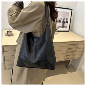 Détail d'un grand sac cabas noir en cuir huilé porté par un mannequin dans une pièce sobre