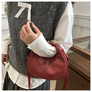 Détail du sac demi-lune tressé rouge foncé avec bandoulière réglable porté par le mannequin