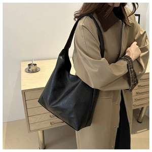 Detail of a large black soft leather hobo bag worn with a beige trench coat