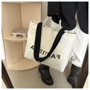 Close-up of a large white canvas tote bag with black letter print and wide black handles