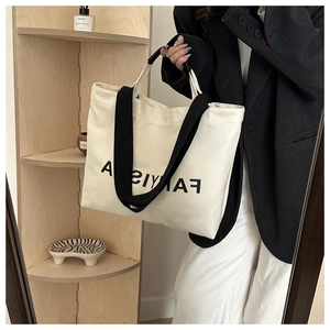 Detail view of cream canvas tote bag with black strap and large letter print on surface