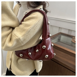 Close-up of deep red glossy underarm bag with silver spherical rivets and sleek texture