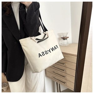 Detailed view of cream canvas tote bag with black handles and shoulder strap on model