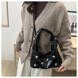 Detail of black patent leather hobo bag with silver metallic rivets worn by a model