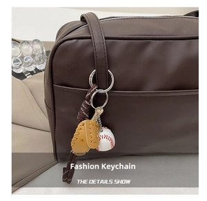 Detail of a baseball and glove pendant hanging on a brown leather shoulder bag
