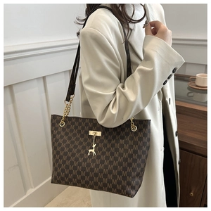 Detail of a brown tote bag with M-pattern print, golden deer charm, and chain strap