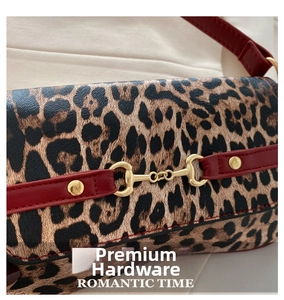 Macro shot of gold horsebit hardware on leopard print bag with red leather trim