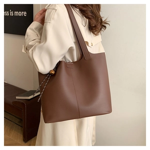 Détail d'un grand sac cabas en cuir marron avec pendentif doré et cordon tressé
