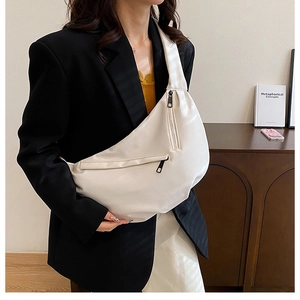 Detail of a large cream crescent crossbody bag with double zippers worn by a model