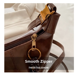 Detail of dark brown leather handbag with golden zipper and woven rope accent