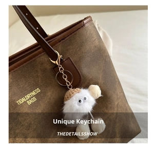 Close-up of white plush monster keychain hanging on a brown leather tote bag with gold hardware