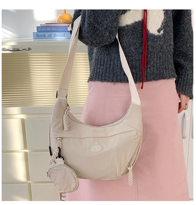 Close-up of beige nylon crescent bag with adjustable strap and round coin purse detail