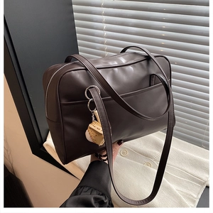 Detail view of dark brown faux leather tote bag with a baseball glove charm on knitwear