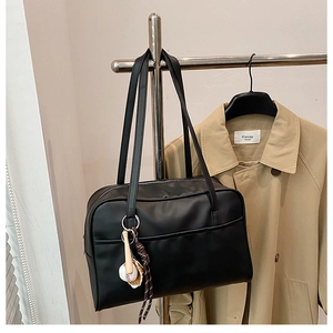 Detail of black tote bag featuring a decorative baseball keychain and slim shoulder straps